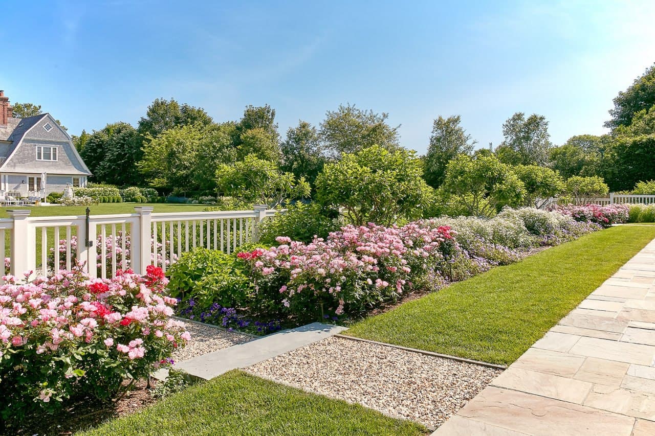 Pink and red rose and peony border along a white picket fence.