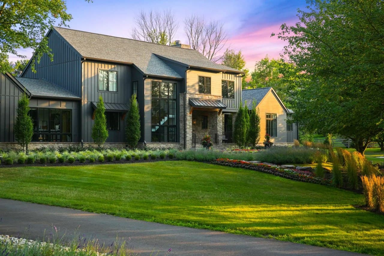 Front facade of a dark-clad estate at dusk with glowing window lights.