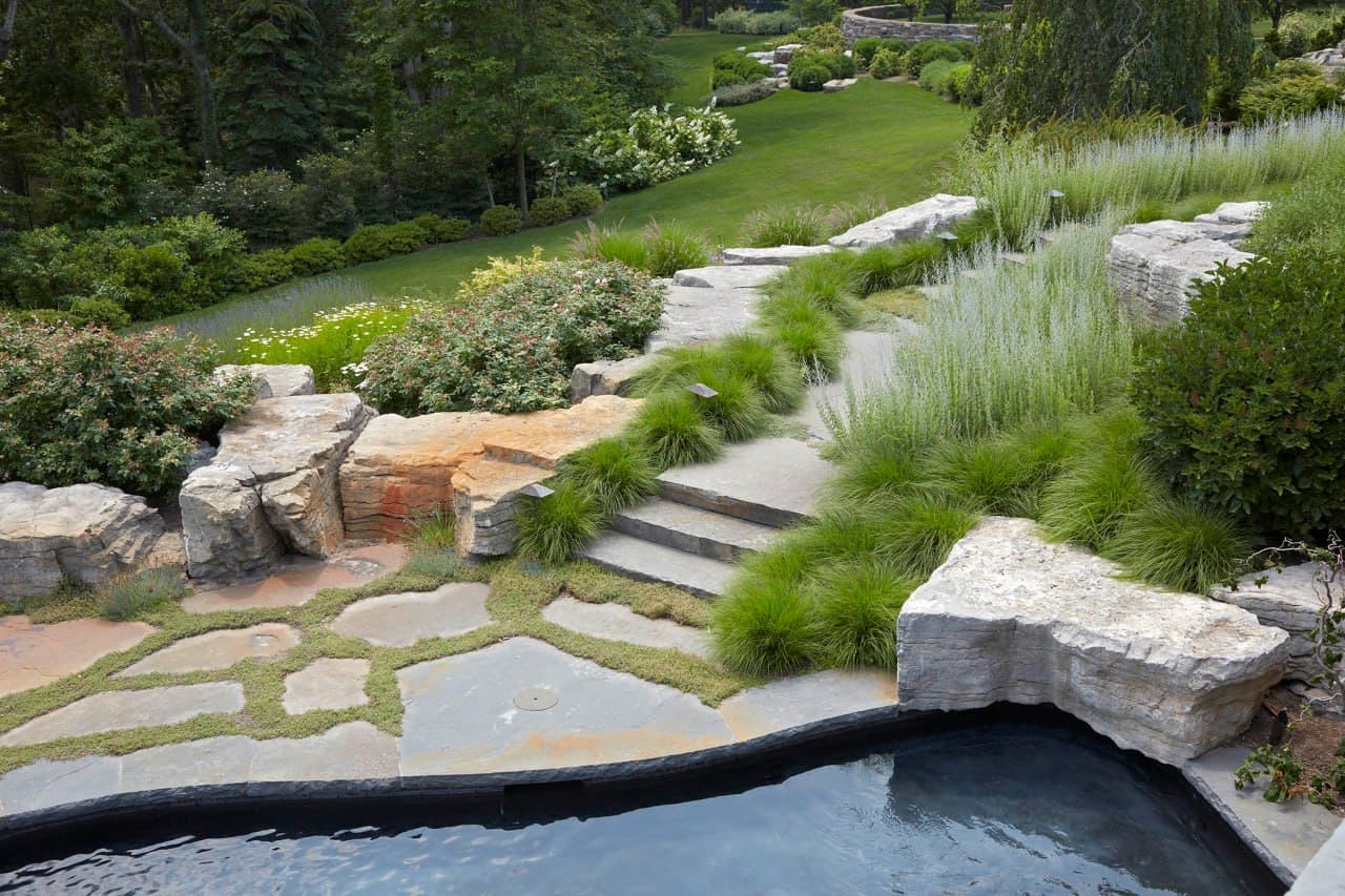 Stone steps through fountain grasses leading down past a plunge pool.