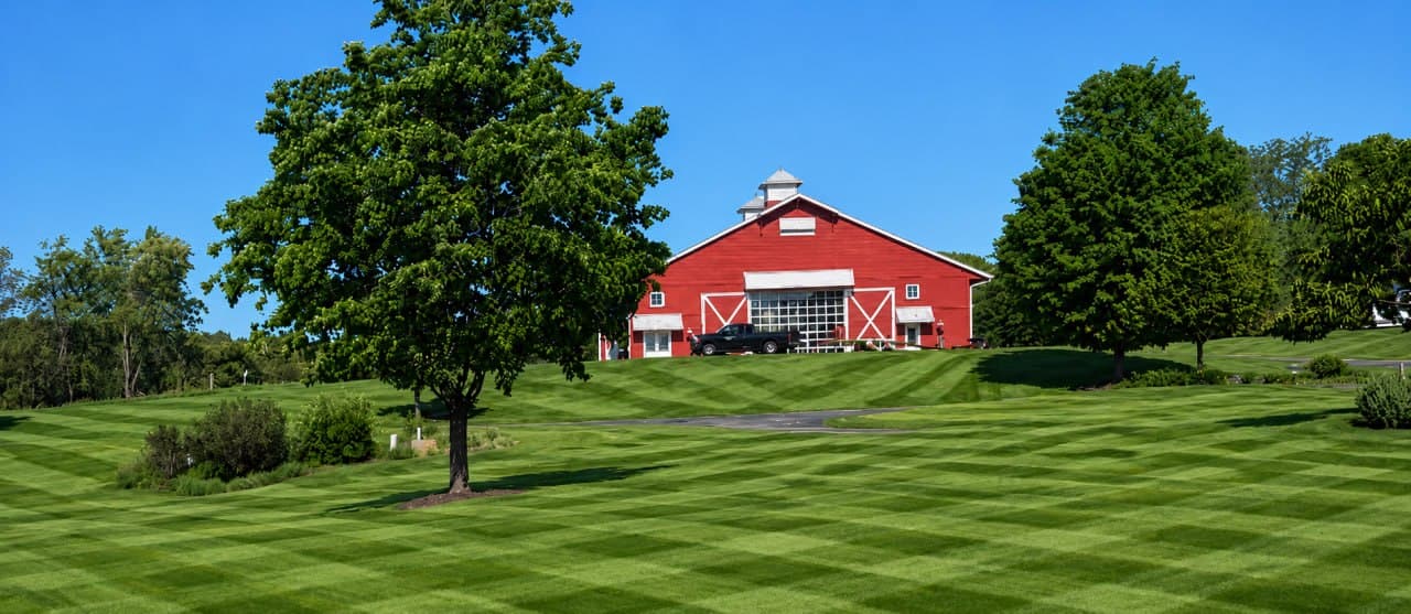 Red barn flanked by mature shade trees on the same estate, fronted by a striped lawn.