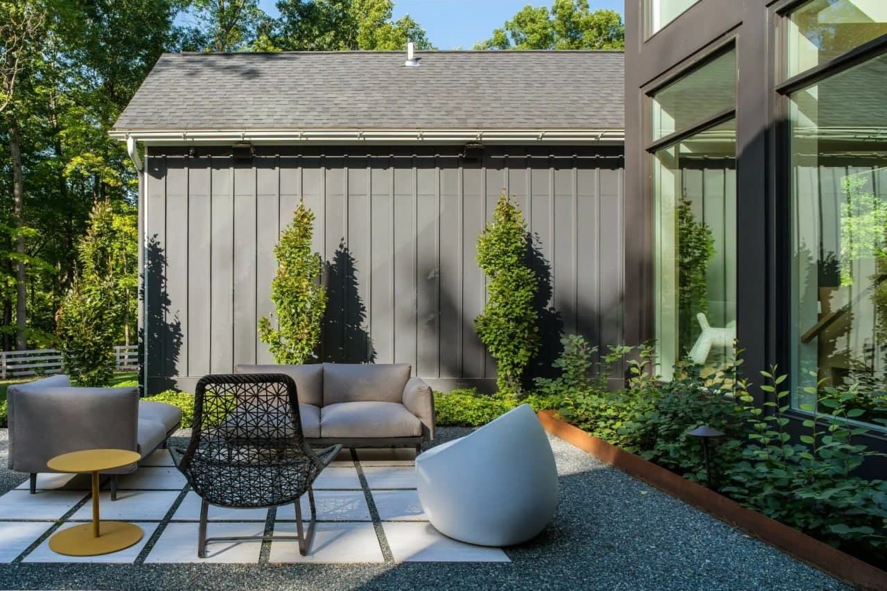 Modern courtyard patio with sculptural furniture beside a board-and-batten home.
