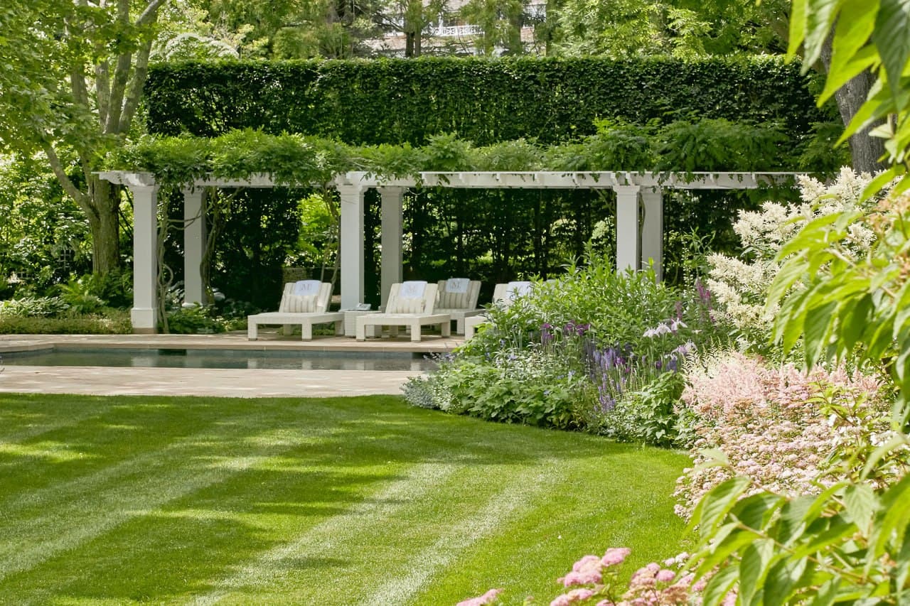 Classic pergola, pool, and layered planting beds beside a residence.