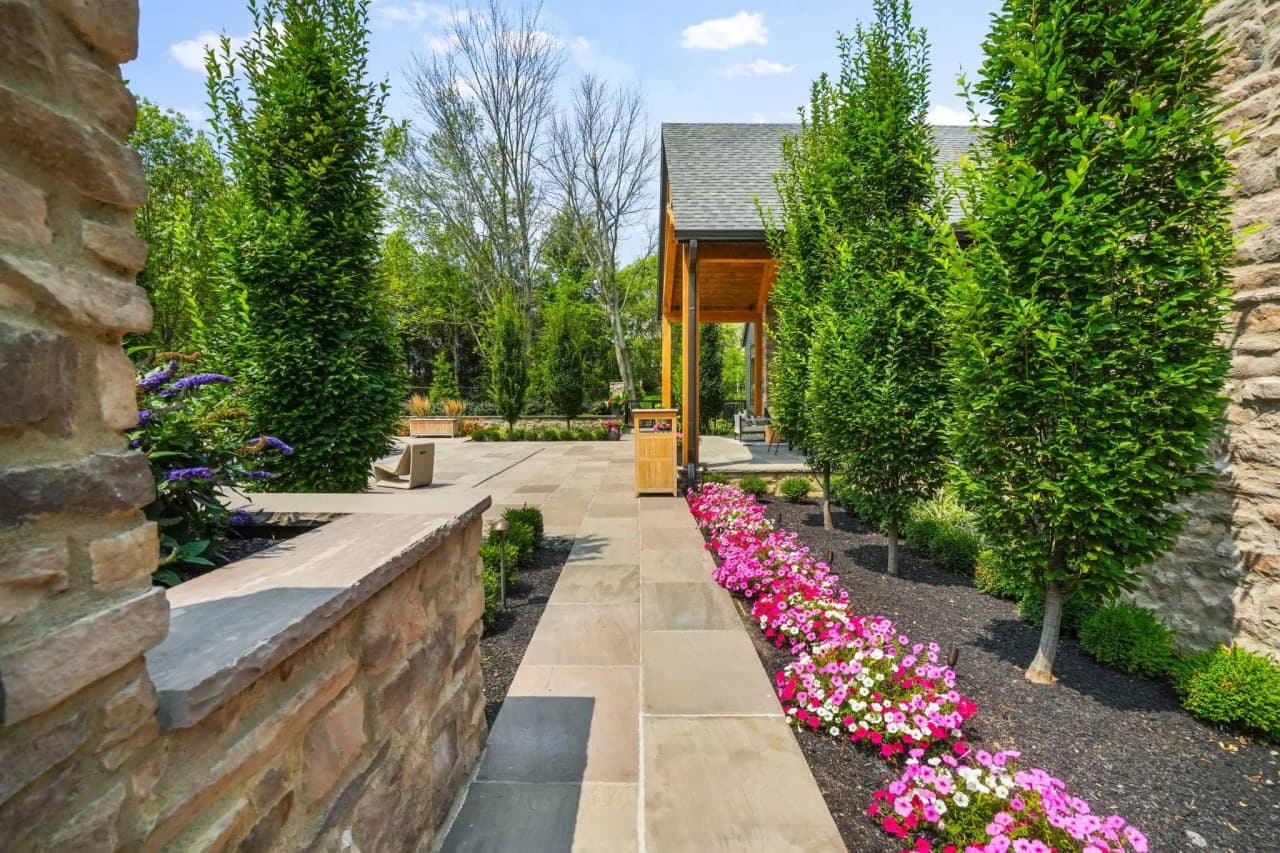 Bluestone path through pink petunia borders with columnar trees.