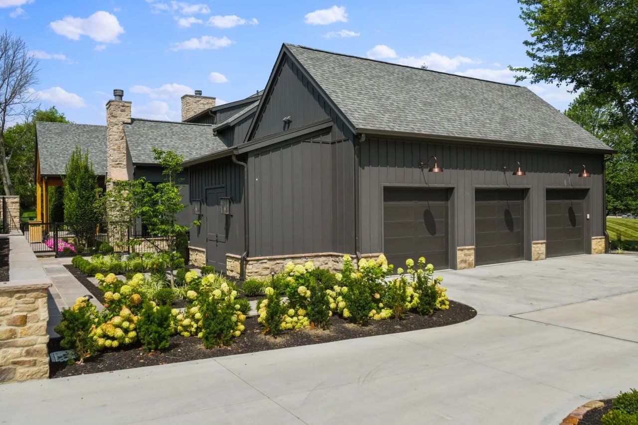 Dark board-and-batten home with paniculata hydrangea garage bed.
