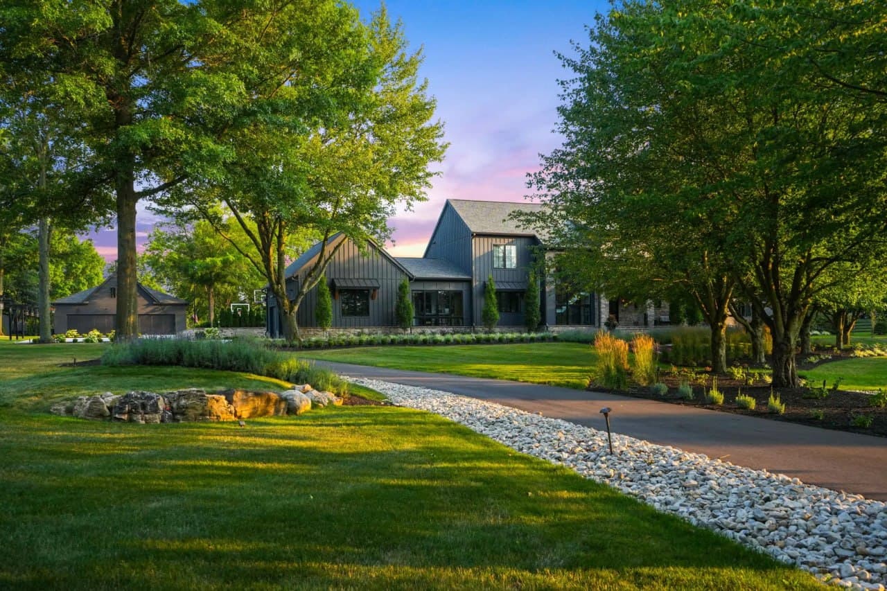 Dark-clad modern estate with rock-bed drive at sunset.