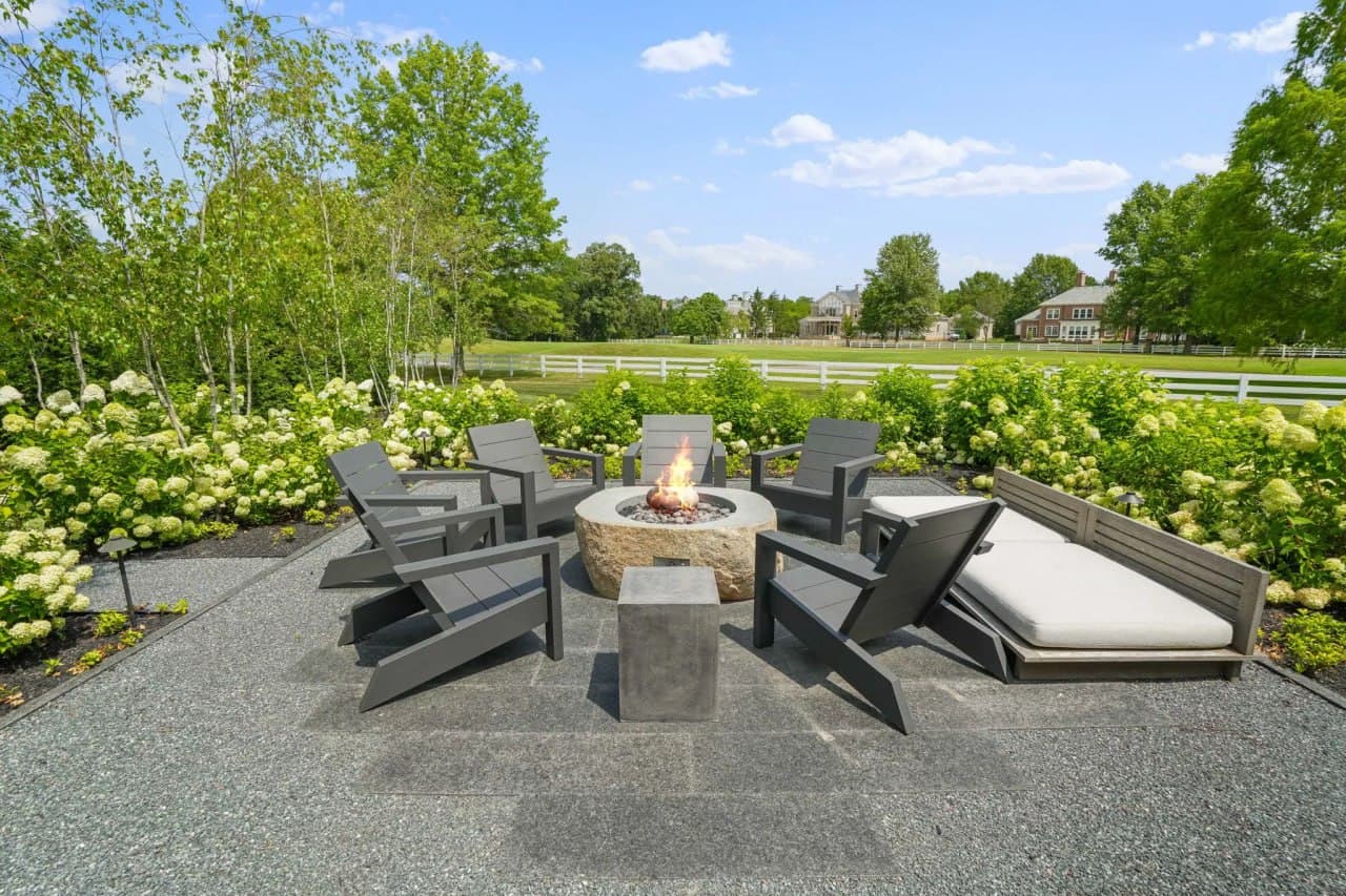 Modern firepit surrounded by hydrangeas and a white picket fence.