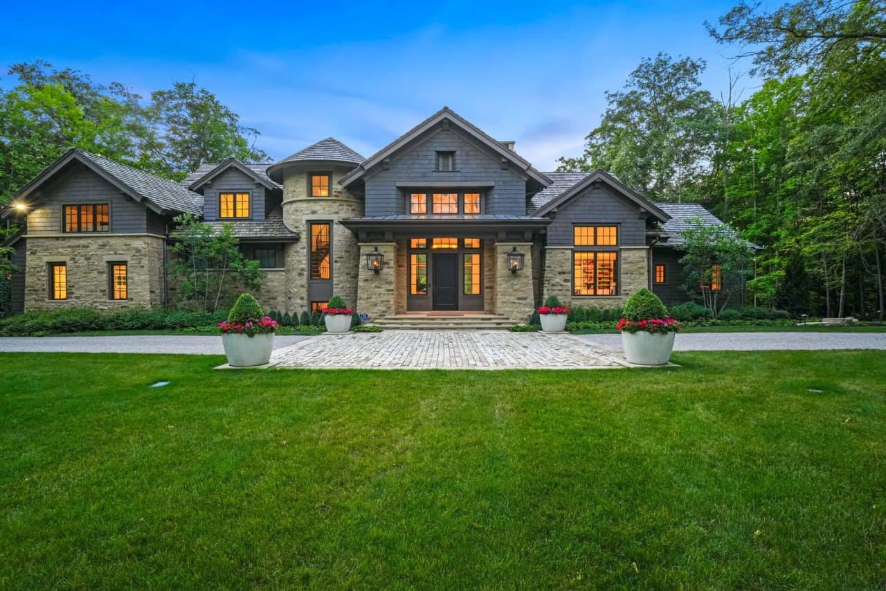 Cedar-shingle estate at dusk with windows glowing warm against a blue sky.