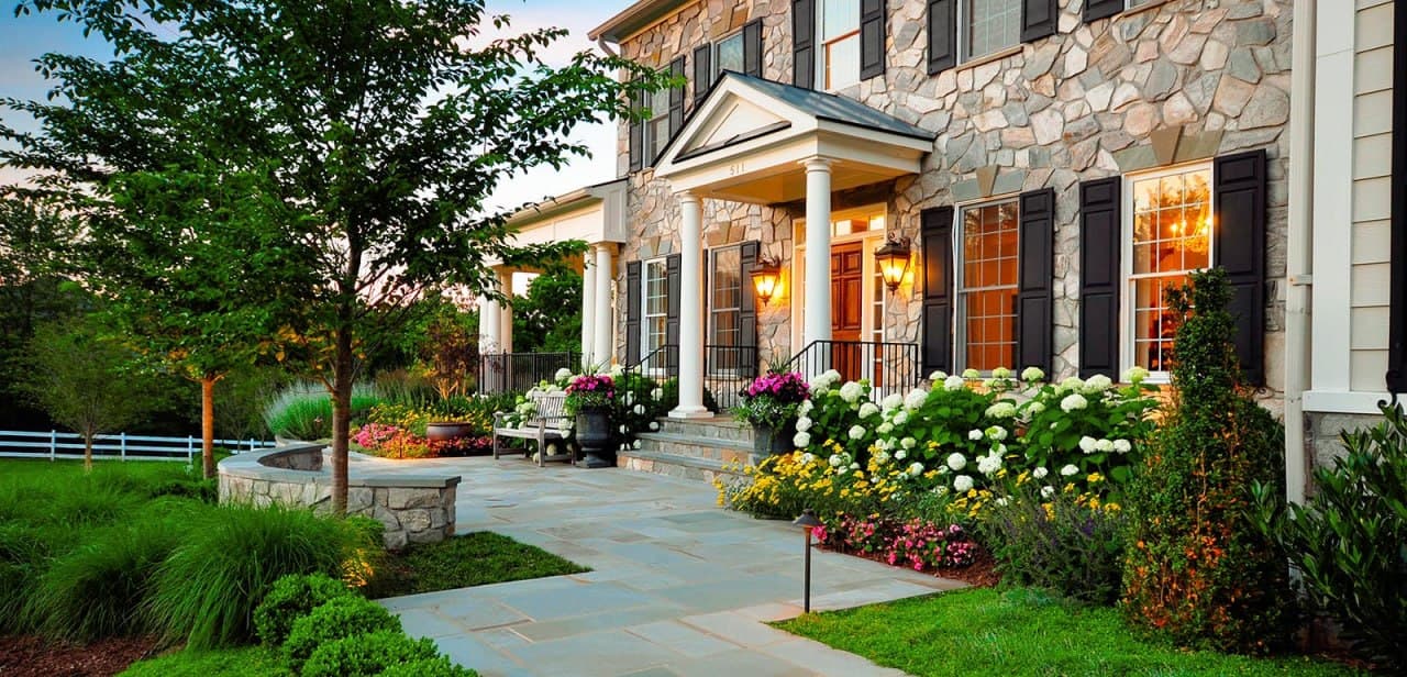 Stone-front estate at golden hour with mature plantings and walkway